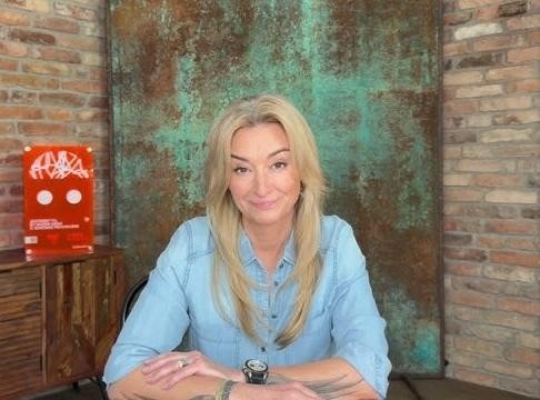 Martyna Wojciechowska – zbliżenie na twarz, z determinacją i empatią, na rozmytym tle symbolizującym jej podróże.