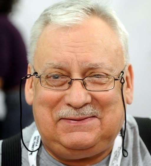 Tłum ludzi na targach książki, przeglądający fantastykę, z subtelnymi nawiązaniami do Wiedźmina.