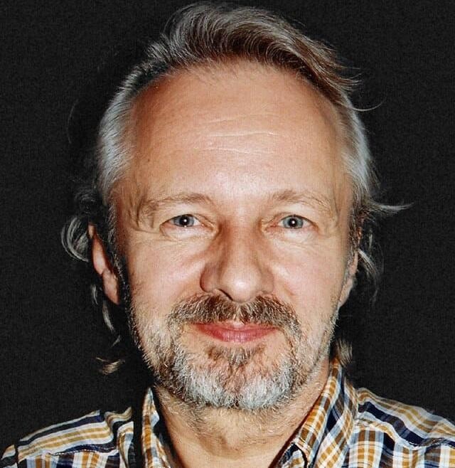 Krzysztof Stroiński uśmiechający się łagodnie w ciepłym, naturalnym otoczeniu.