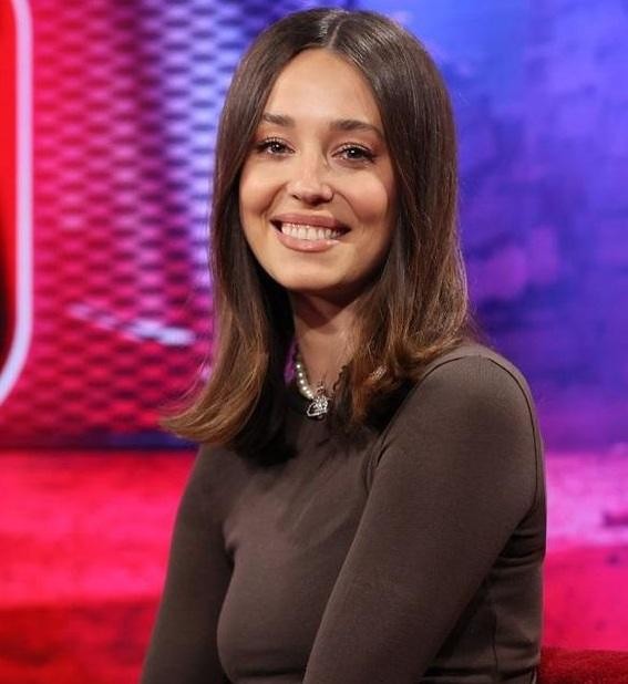 Alt: Izabella Krzan jako prezenterka telewizyjna, aktywnie prowadząca program w studiu, z mikrofonem, uśmiechnięta i gestykulująca, ukazująca swoją pasję do pracy w mediach.