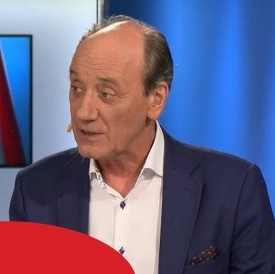 Dariusz Szpakowski w kabinie komentatorskiej, skoncentrowany na monitorze z meczem piłkarskim, z słuchawkami i mikrofonem.
