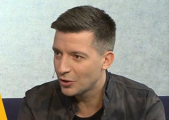 Michał Cessanis podczas prelekcji „Kamperem przez Australię Zachodnią”, z dynamiczną prezentacją australijskiego krajobrazu w tle, gestykulujący z pasją do publiczności.