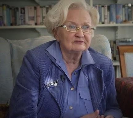 Ewa Łętowska zamyślona nad książką, w otoczeniu regałów pełnych tomów, symbolizujących jej pasję do nauki i literatury.