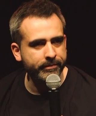 Abelard Giza na scenie z mikrofonem, energicznie gestykulujący podczas występu stand-upowego.