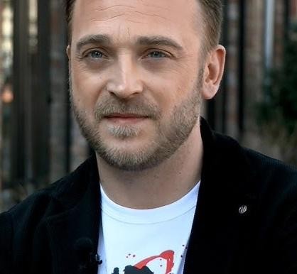 Mateusz Gessler gotujący w profesjonalnej kuchni, z uśmiechem i zaangażowaniem, w tle widać nowoczesny sprzęt kuchenny.