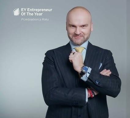 Rafał Brzoska w zamyśleniu, w tle biura, symbolizujący jego życie prywatne i zaangażowanie w biznes.