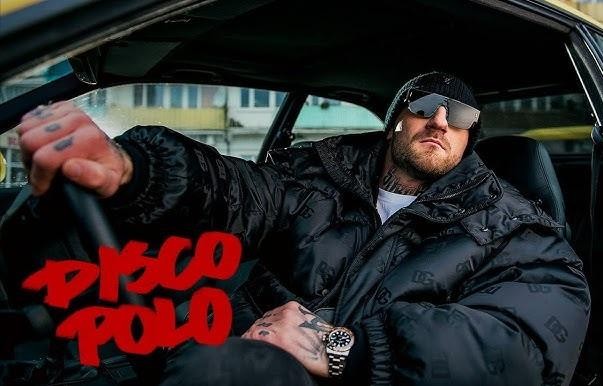Kizo, Patryk Woziński, w dynamicznej pozie podczas walki Fame MMA, ubrany w strój sportowy, z rozmytym tłem klatki i publiczności.